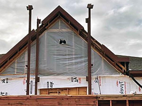 a peaked roof of a building has plastic protecting the interior and steel columns in front of it